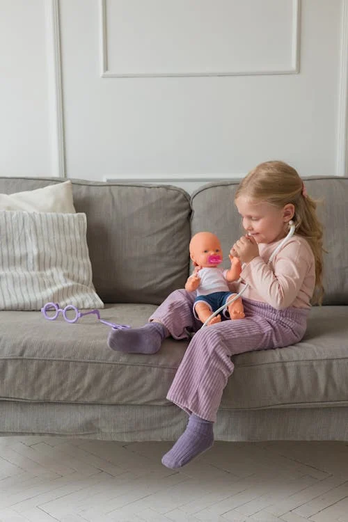 Enfant qui joue à la poupée assise sur un canapé