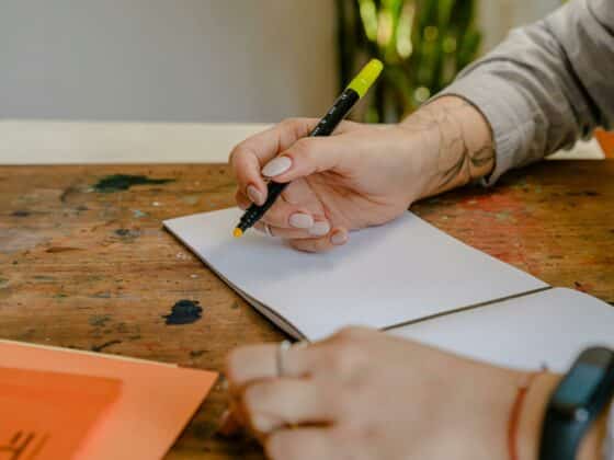 Image d'une main qui tient un feutre jaune au dessus d'un cahier