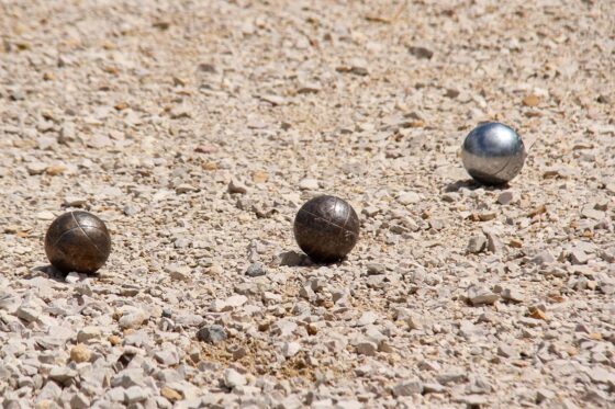 image de 3 boules de pétanques posés sur un sol en caillou.