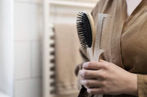 Image d'une dame qui tient dans sa main une brosse à cheveux avec un manche en bois et un peigne.