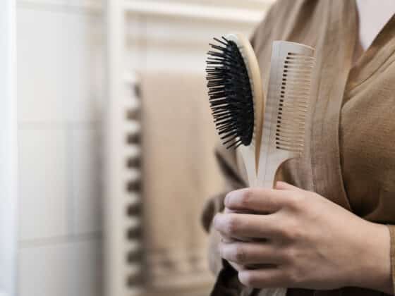 Image d'une dame qui tient dans sa main une brosse à cheveux avec un manche en bois et un peigne.