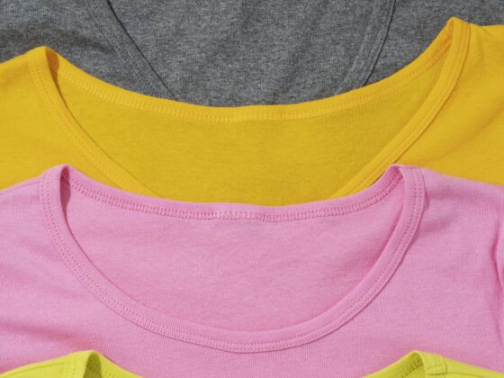 Image de 4 t-shirts de couleurs (gris, orange, rose et jaune) empilés.