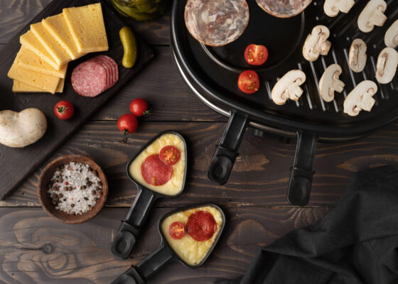 Image d'un appareil et des ustensiles à raclette posé sur la table avec un assortiment de nourriture à côté