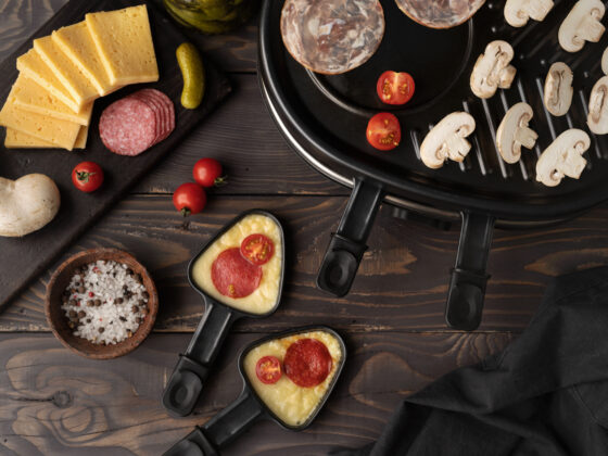 Image d'un appareil et des ustensiles à raclette posé sur la table avec un assortiment de nourriture à côté